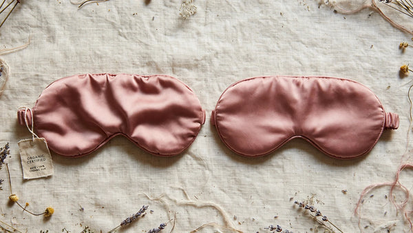 Deux masques de sommeil en soie rose poudré côte à côte, l'un avec une étiquette bio certifiée