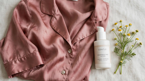 Pyjama en soie rose poudré posé a plat a cote d une lotion douce sans parfum et d un brin de camomille